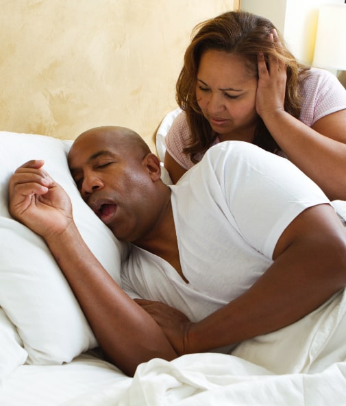 Woman frustrating in bed next to snoring man