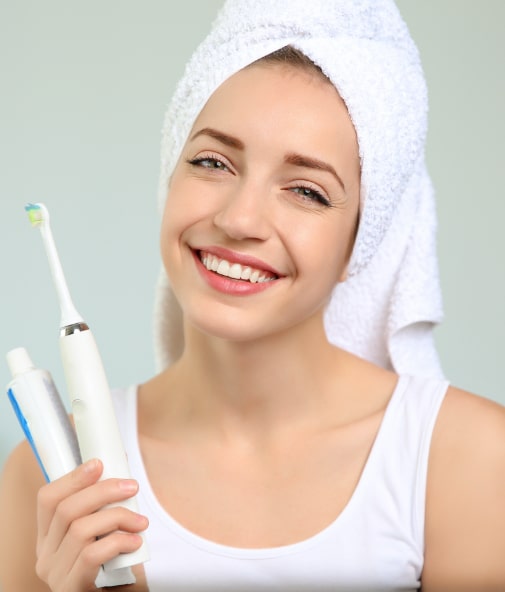 Woman smiling and holding up toothbrush used to care for her porcelain veneers